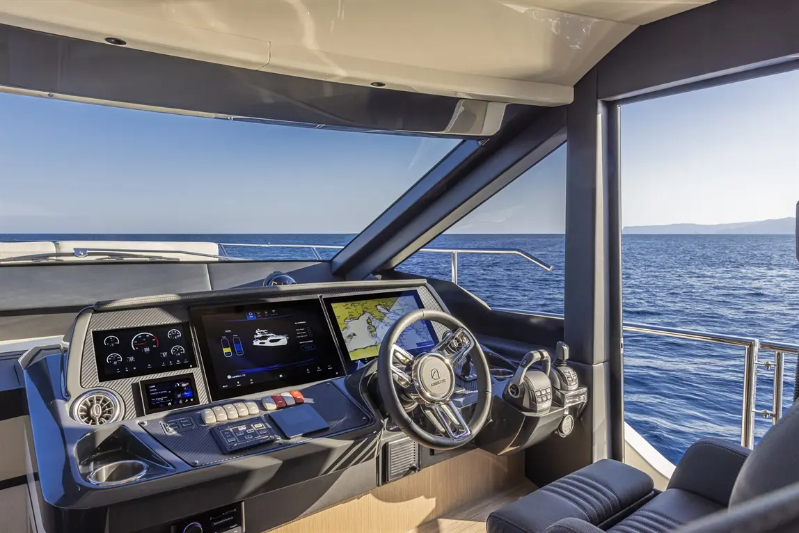 Luxurious yacht cockpit featuring a steering wheel, digital displays, and scenic ocean view through large windows.
